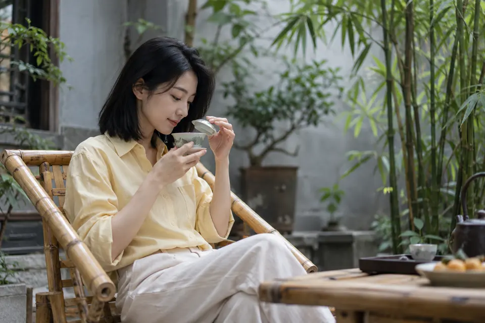 竹影院落中，年轻女性用盖碗闻香品茶